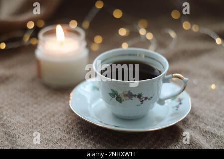 Détails de la nature morte dans l'intérieur de la maison du salon. Pull, tasse de thé, coton, confortable, bougie. Moody. Mug, bougies et une guirlande bokeh sur un sombre Banque D'Images