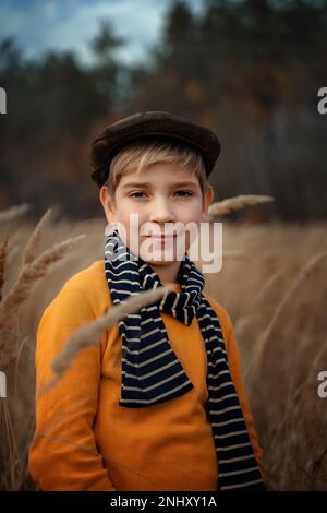 Un petit garçon souriant dans une casquette rétro se tient et sourit. Mode pour enfants, style rétro. Banque D'Images