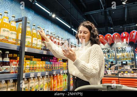 une femme achète du jus d'une liste d'épicerie sur son téléphone dans un supermarché Banque D'Images