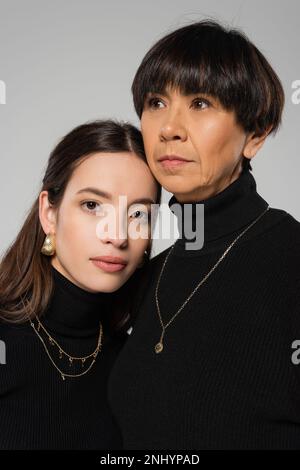 portrait de la jeune femme asiatique et de la mère d'âge moyen en mouchetures noires et colliers isolés sur le gris Banque D'Images