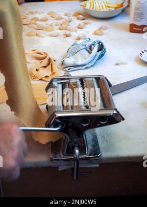 caucasien homme senior pâte roulante à main pour pâtes maison non cuites de machine italienne dans les mains avec la farine de semoule sur la texture de marbre blanc Banque D'Images