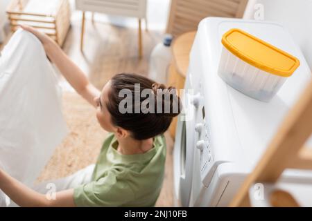 Vue en hauteur de la femme de brunette tenant des vêtements propres près de la machine à laver dans la buanderie, image de stock Banque D'Images