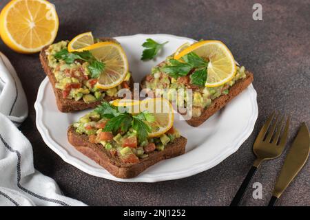 Les sandwichs Guacamole faits maison sont garnis de citron sur une assiette blanche sur fond marron Banque D'Images