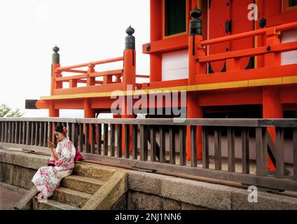 Kyoto, Japon - sept, 2017: Jeune femme touriste assis avec un kimono sur le site du temple de Kiyomizu dera, devant un bâtiment en bois orange Banque D'Images
