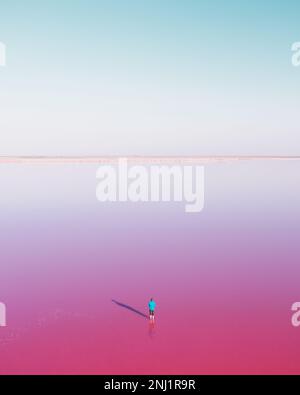 Homme solitaire en bleu junked dans l'eau de lac rose sous ciel bleu clair en été. Concept de couleur créative Banque D'Images