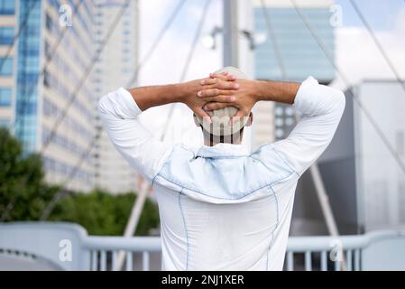 Image arrière de l'homme avec ses mains sur la tête en regardant vers la ville. Banque D'Images