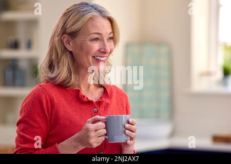 Femme mûre souriante debout dans la cuisine se détendre avec une tasse de café Banque D'Images