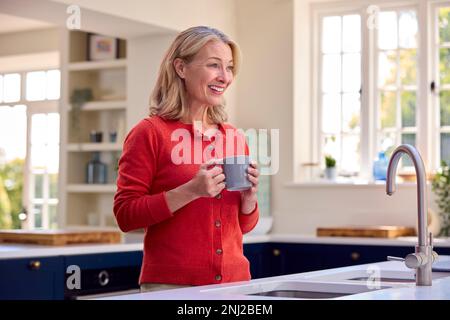 Femme mûre souriante debout dans la cuisine se détendre avec une tasse de café Banque D'Images