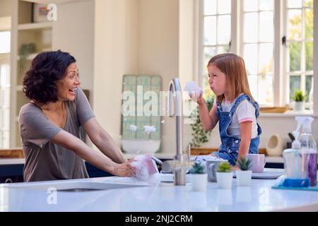 Famille avec fille aidant la mère plus âgée à faire laver dans la cuisine à la maison bulles de savon soufflantes Banque D'Images