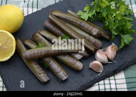 Palourdes fraîches au rasoir, à l'ail, au persil et au citron, sur une assiette en ardoise noire. Une présentation parfaite pour une expérience de fruits de mer authentique. Banque D'Images