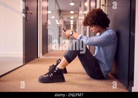 Jeune femme d'affaires stressée assise au sol dans le couloir du bureau moderne avec téléphone Banque D'Images