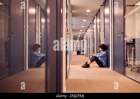 Jeune femme d'affaires stressée assise au sol dans le couloir du bureau moderne avec téléphone Banque D'Images