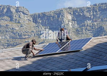Équipe d'installation de panneaux solaires, d'onduleurs et de batteries de secours reliés au réseau hybride pour lutter contre la charge en Afrique du Sud. Banque D'Images