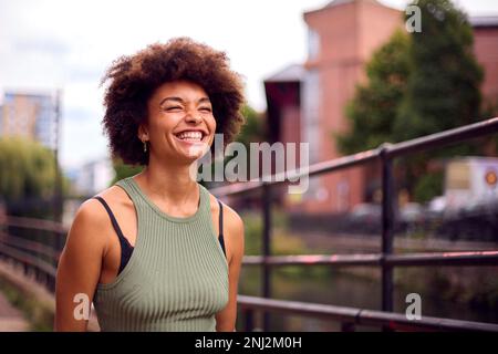 Souriante jeune femme en plein air riant pendant qu'elle marche à travers la ville Banque D'Images