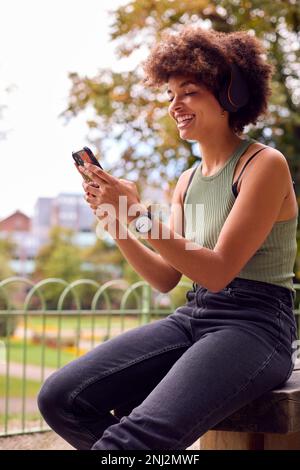 Jeune femme à l'extérieur portant un casque sans fil Streaming Show à partir d'un téléphone mobile Banque D'Images