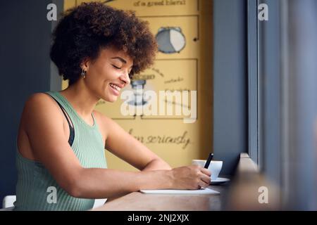 Femme dans la fenêtre du café travail écriture dans le cahier Banque D'Images