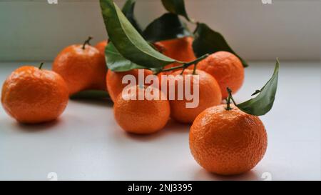 mandarines mûres au pelage et avec des feuilles sur une table blanche, agrumes en vrac sur une surface légère, clémentines parfumées comme fond alimentaire Banque D'Images