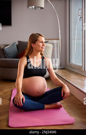 Femme enceinte portant des vêtements de fitness sur un tapis d'exercice à la maison faisant du yoga Banque D'Images