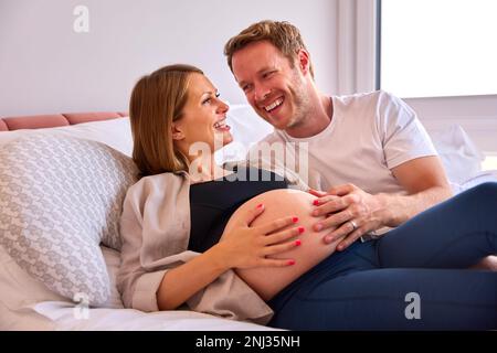 Couple aimant à la maison allongé sur le lit avec l'homme touchant le ventre de la femme enceinte Banque D'Images