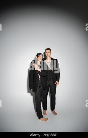 couple multiethnique pieds nus dans des pantailleurs élégants noirs sur fond gris, image de la banque Banque D'Images