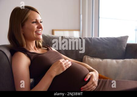 Femme enceinte se détendant sur un canapé à la maison tenant l'estomac Banque D'Images