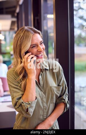 Femme d'affaires mature debout près de la partition dans le plan ouvert Bureau faire un appel sur téléphone mobile Banque D'Images