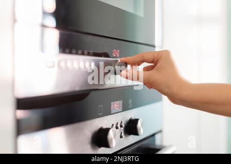 Femme règle la température à la main sur le four électrique pendant la cuisson dans la cuisine Banque D'Images