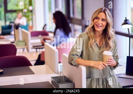 Femme d'affaires mature debout près de la partition dans le bureau à plan ouvert avec boisson de Takeaway Banque D'Images
