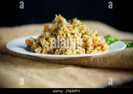 boulgour cuit avec des légumes, des carottes et des champignons séchés dans une assiette sur une table en bois. Banque D'Images