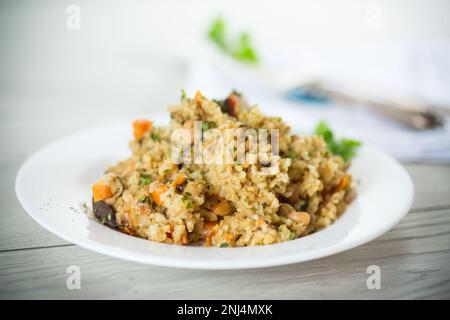 boulgour cuit avec des légumes, des carottes et des champignons séchés dans une assiette sur une table en bois. Banque D'Images