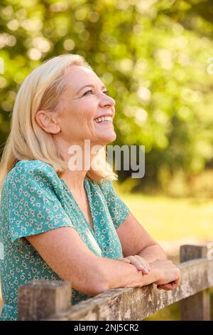 Portrait d'une femme mûre ou sénior vêtue à la légère penchée sur Fence lors d'une promenade à la campagne Banque D'Images