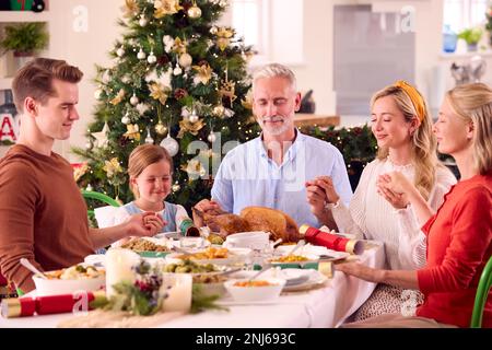 Famille de plusieurs générations célébrant Noël à la maison en disant prière avant de manger ensemble Banque D'Images