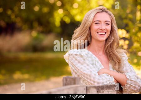 Jeune femme vêtue de façon décontractée penchée sur Fence lors d'une promenade à la campagne Banque D'Images