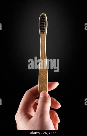 Brosse à dents écologique en bambou dans la main d'une femme sur fond sombre. Concepts de consommation responsable. Banque D'Images