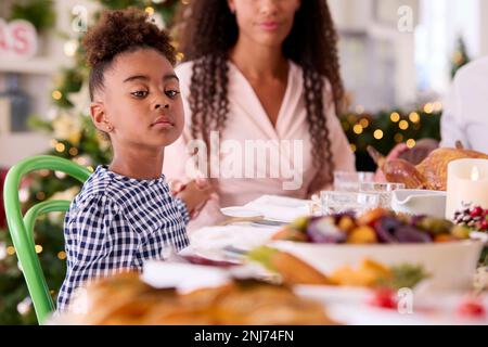 La famille fête Noël à la maison avec mère et fille disant prière avant de manger Banque D'Images