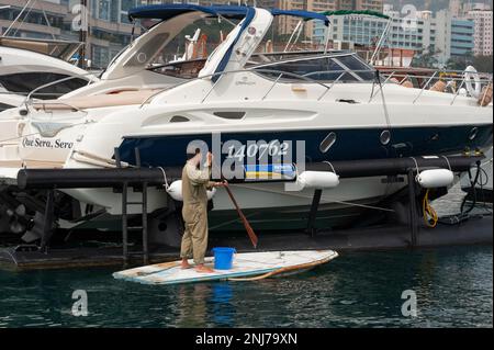 Un homme sur une sorte de stand-up paddle board fait son chemin entre les yachts de luxe dans le port d'Aberdeen, Hong Kong. Banque D'Images