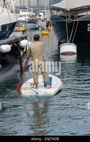 Un homme sur une sorte de stand-up paddle board fait son chemin entre les yachts de luxe dans le port d'Aberdeen, Hong Kong. Banque D'Images