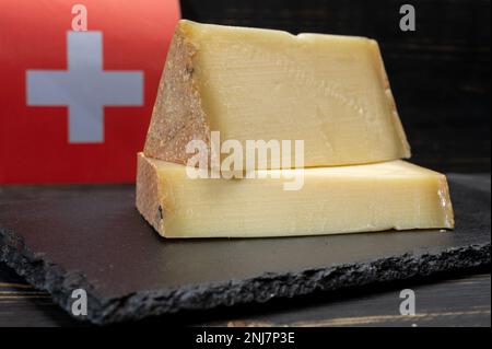 Fromage suisse de lait de vache moyen dur Gruyere, appenzeller utilisé pour la fondue au fromage traditionnel et le gratin et le drapeau de la Suisse sur fond sombre Banque D'Images