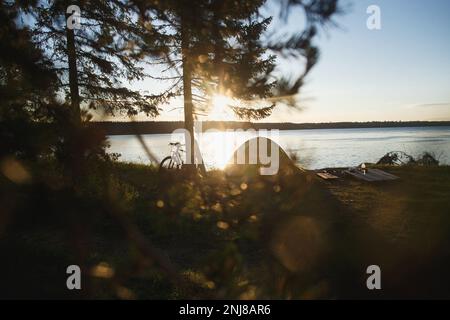 Tente, vélo et magnifique camping avec rivière au lever du soleil. Concept de cyclisme de tourisme. Banque D'Images