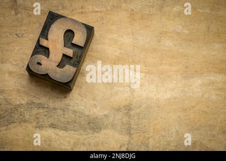 Le symbole livre sterling britannique en forme de bloc d'impression de type bois de typographie contre du papier artisanal en écorce avec un espace de copie Banque D'Images