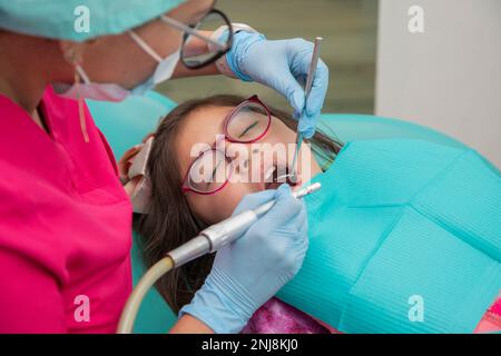 fille avec sa bouche ouverte tandis que son dentiste nettoie ses dents avec une pièce à main contra-angle Banque D'Images