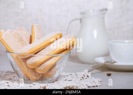 Biscuits italiens traditionnels savoiardi ou ladyfingers dans un bol en verre et morceaux de biscuits et de sucre sur la table, une tasse de café blanc avec une cuillère Banque D'Images