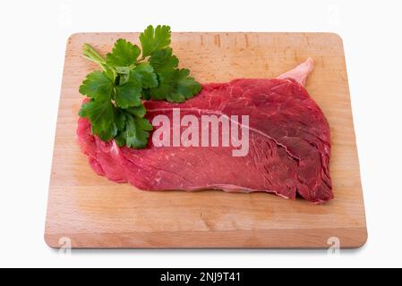 Steak de bœuf cru sur planche à découper en bois avec feuilles de persil isolées sur blanc avec passe-cheveux Banque D'Images