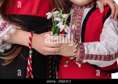 Garçons et filles bulgares en costumes traditionnels folkloriques avec fleurs printanières en forme de goutte d'eau et bracelet en laine martenitsa, symbole de Baba Marta Banque D'Images
