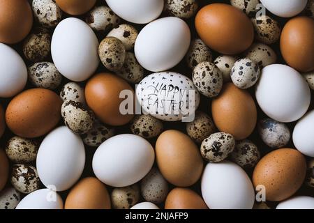 Joyeux pâques écrit blanc oeuf de poulet sur pile d'oeufs. Pile d'œufs de poulet brun et blanc avec œufs de caille Banque D'Images