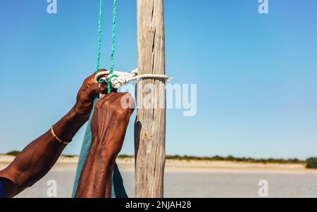 Homme malgache local fixant la corde de voile à un poteau en bois de son navire, détail aux mains seulement Banque D'Images