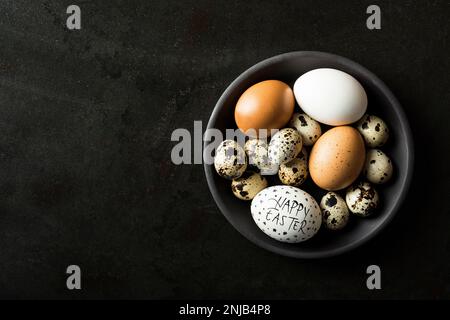 Œufs de poulet blancs et bruns avec des œufs de caille dans un bol sur fond rustique de métal noir Banque D'Images