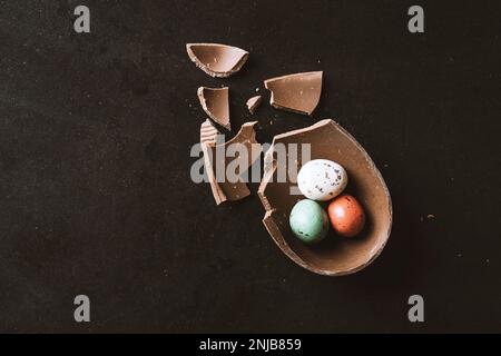Œuf de chocolat de pâques craqué plein de petits œufs de chocolat sur fond noir Banque D'Images