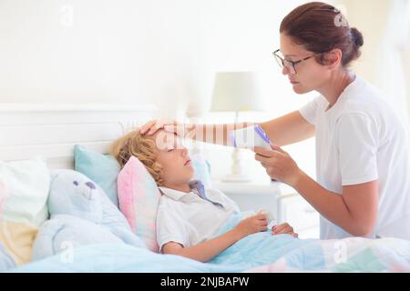 Enfant malade au lit. La mère s'est mise à vérifier sur un enfant malin. Un petit garçon qui a de la fièvre se sent malade. Maman avec thermomètre et médicaments contre la toux. Banque D'Images