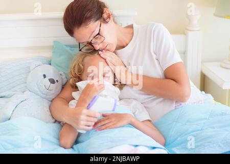 Enfant malade au lit. La mère s'est mise à vérifier sur un enfant malin. Un petit garçon qui a de la fièvre se sent malade. Maman avec thermomètre et médicaments contre la toux. Banque D'Images